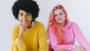 Happy diverse teenagers in bright outfit smiling and looking at camera on white background of studio