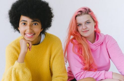 Happy diverse teenagers in bright outfit smiling and looking at camera on white background of studio
