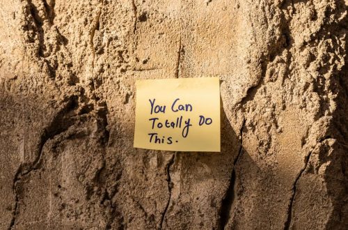 A sticky note with a motivational message on a textured wall in Dubai, with sunlight casting shadows.