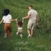 A joyful family strolls through a lush green field, enjoying quality time together.